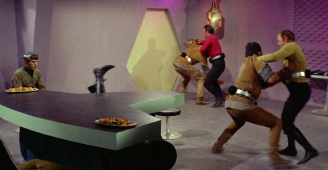 Kirk and Scotty fight two men while brainless Spock sits perfectly still at a table.