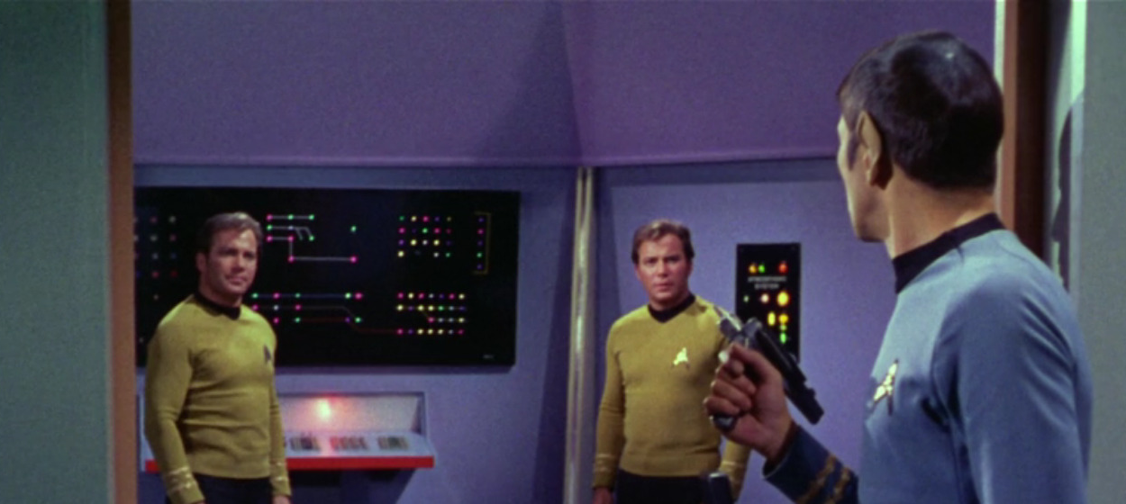 Spock stands in a doorway with a phaser, looking at Kirk and a shapeshifter disguised as Kirk.
